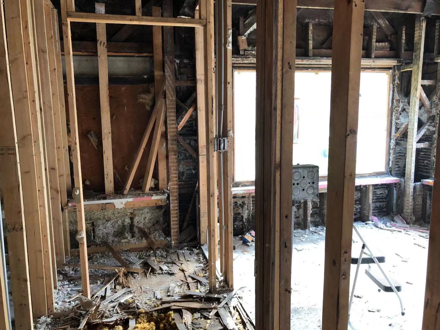 Wood lath stripped from interior wall, exposing brick chimney structure with debris on the floor.